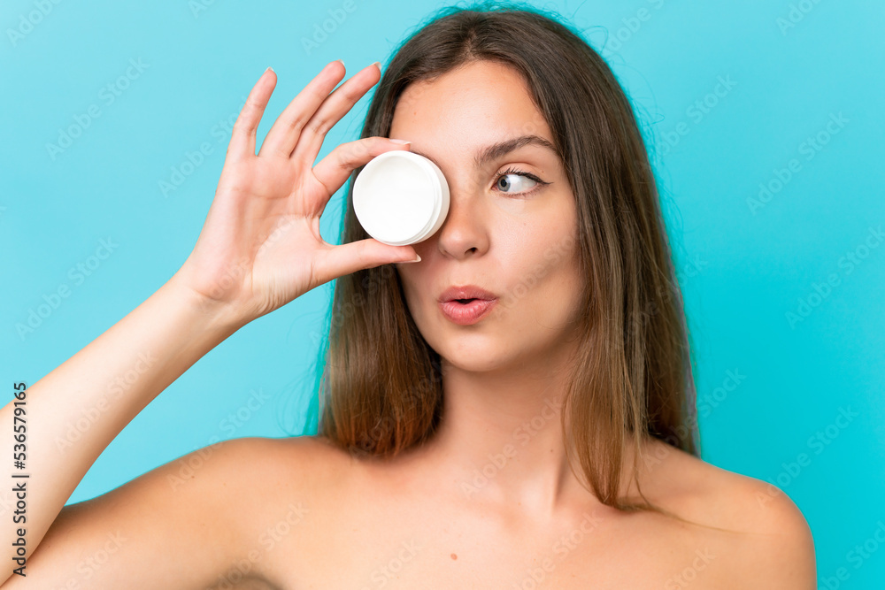 Young caucasian woman isolated on blue background with moisturizer and surprised Young caucasian woman isolated on blue background with moisturizer and surprised