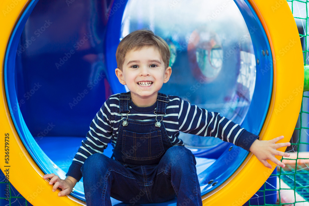Little boy toddler smiles at the camera. He plays in the game center. Climbs the pipe Little boy toddler smiles at the camera. He plays in the game center. Climbs the pipe