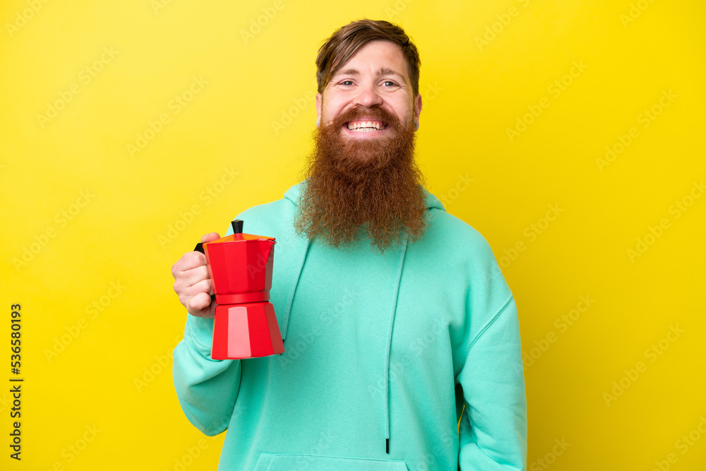 Redhead man with beard holding coffee pot isolated on yellow background smiling a lot Redhead man with beard holding coffee pot isolated on yellow background smiling a lot