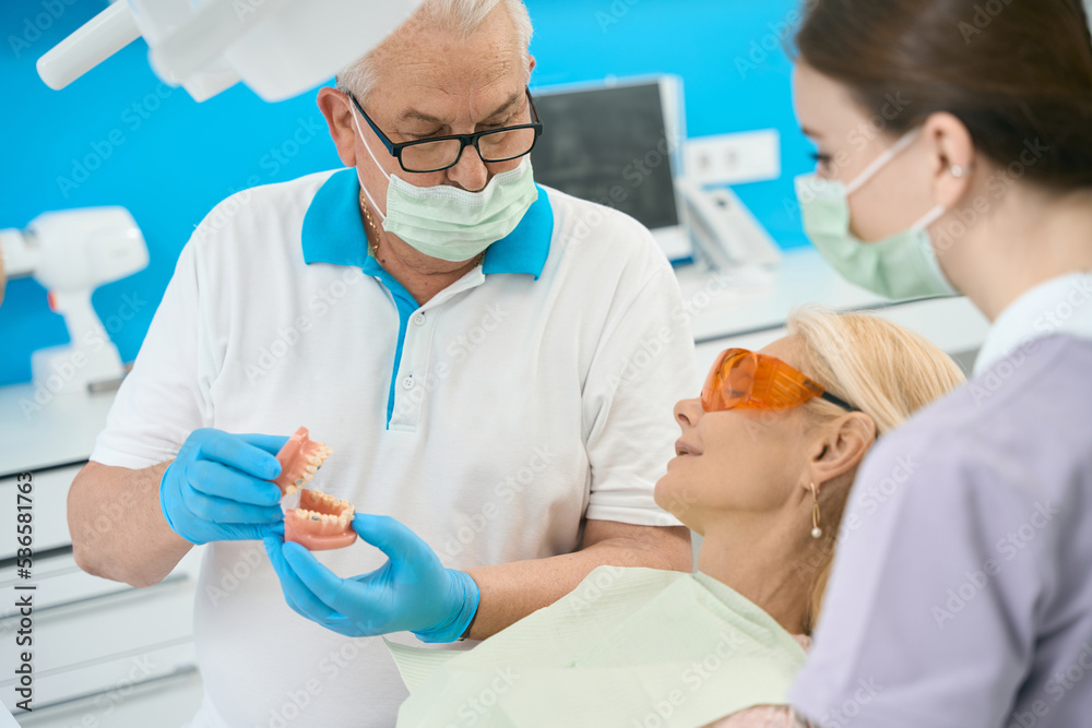 Seriously dentist in glasses with artificial jaw with braces in dental clinic Seriously dentist in glasses with artificial jaw with braces in dental clinic