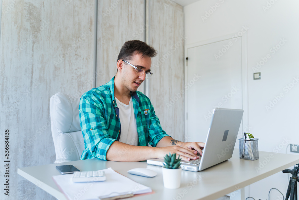 A young guy doing business work in his home office during the day while talking on phone using laptop and his mobile phone
A young guy doing business work in his home office during the day while talking on phone using laptop and his mobile phone