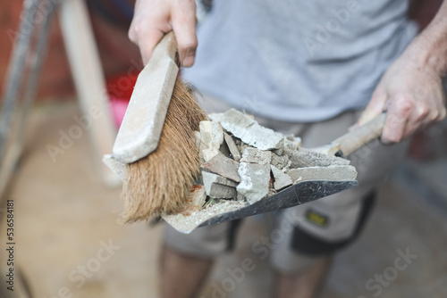 A young Caucasian man holds a scoop with construction waste and a broom to throw it into a bag