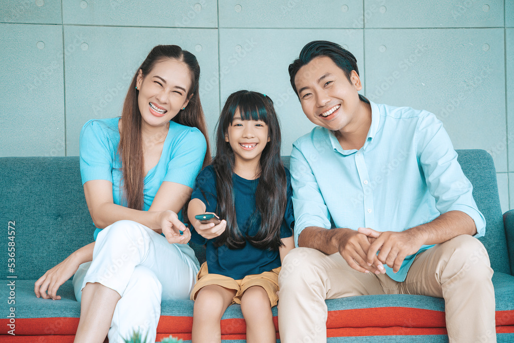 Happy Asian family lifestyle enjoy watching TV in living room at home. Happy Asian family portrait with mother, father and daughter