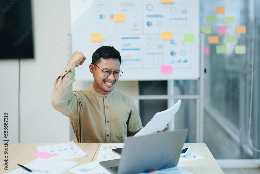 Portrait of a male business owner showing a happy smiling face as he has successfully invested his business using computers and financial budget documents at work Portrait of a male business owner showing a happy smiling face as he has successfully invested his business using computers and financial budget documents at work