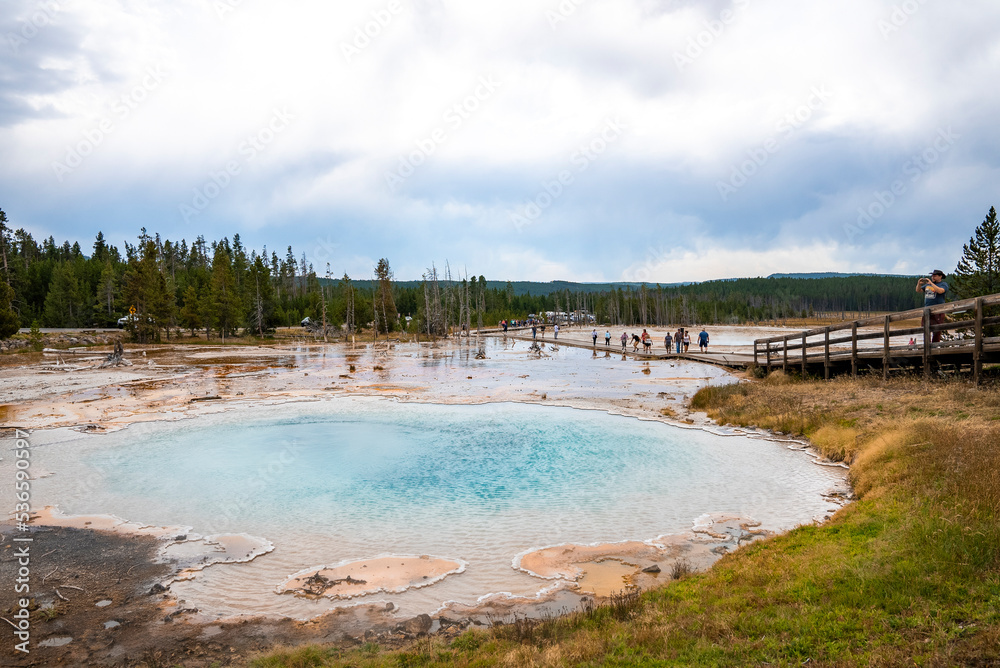 Fototapeta premium Tourists exploring Silex spring at national park. Travelers visiting hot thermal pool in forest. Beautiful scenery of famous tourist attraction with cloudy sky in background.