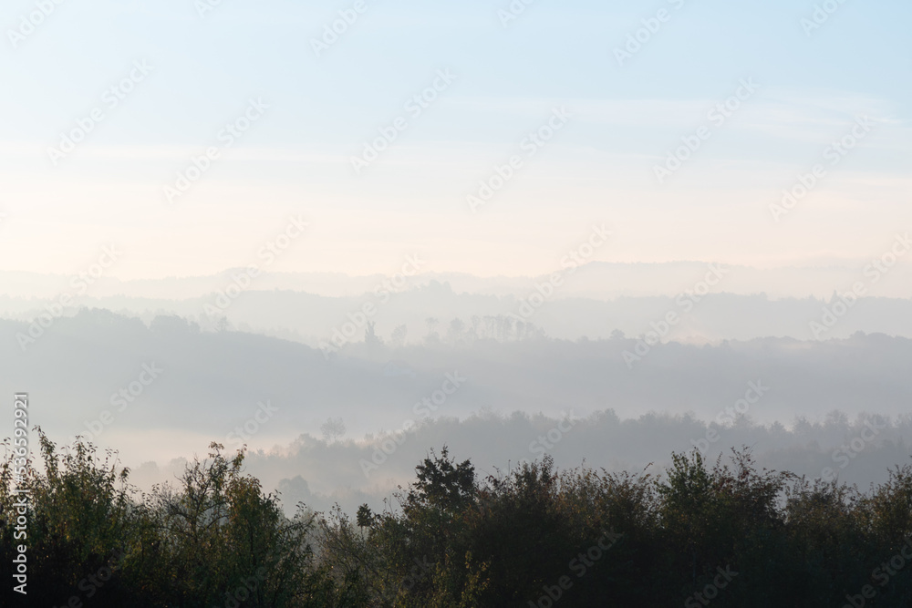 Fototapeta premium Hills with forest in fog at autumn morning, misty forest layers in autumn
