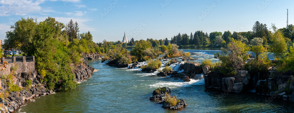 Panoramic view of scenic Idaho falls and Snake river. Beautiful tourist attraction in city. Picturesque natural scenery of flowing water amidst rocks and plants with sky in background.