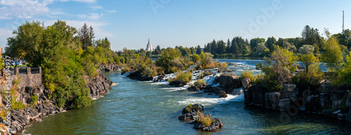 Panoramic view of scenic Idaho falls and Snake river. Beautiful tourist attraction in city. Picturesque natural scenery of flowing water amidst rocks and plants with sky in background.