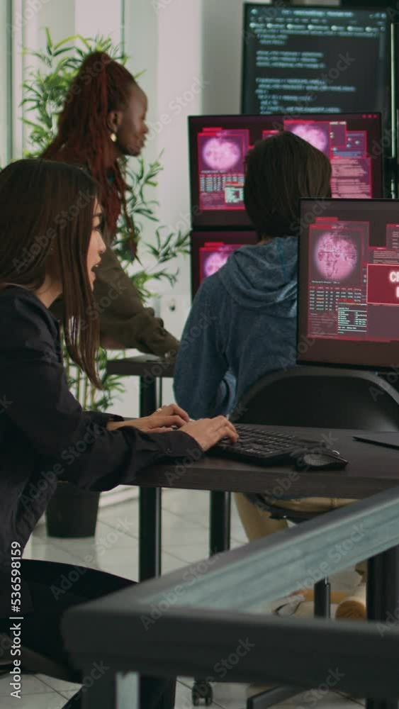 Vertical video: Team of system engineers having web server hacked, reading critical error on multiple monitors in office. Diverse software developers trying to solve hacking problem, firewall security
