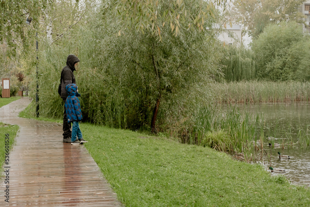 a man with a child in a jacket with a hood, stand and look at the lake on a rainy day a man with a child in a jacket with a hood, stand and look at the lake on a rainy day