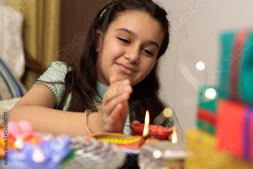 Young girl, kid, dressed up in ethnic lighting diya or lamp with smile expression pose for photo with family in background celebrating diwali Hindu festival Laxmi poojan
