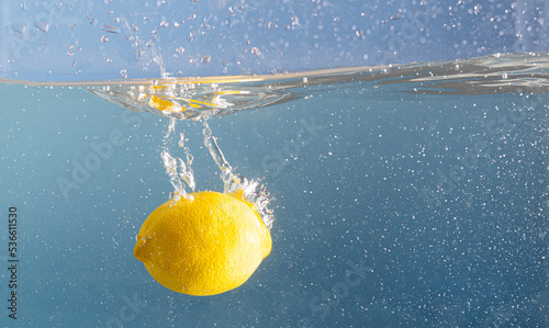 Fresh lemon soaked deep into the splashing blue water. Blue pool water and a fruit motion. Creative summer food concept.