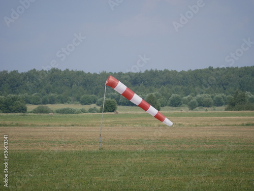 Wind direction and strength indicator on the airfield on a sunny summer day. Synthetic product made of red and white fabric.