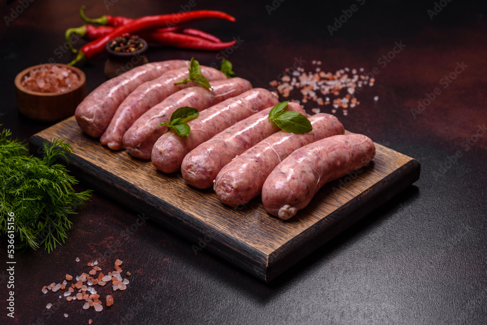 Raw sausages with ingredients on a cutting board on a dark concrete background with copy space