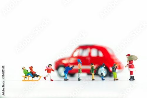 Children stand in line in front of Santa Claus red car in the background