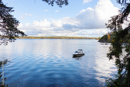 Boat on blue lake under sky with white clouds and coniferous trees around