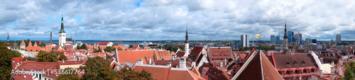 Bird view of historic city center of Tallinn, Estonia. Autumn trees, towers and orange tile roofs of ancient, medieval houses under cloudy overcast Northern sky. Baltic sea on the horizon.