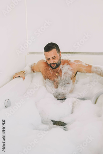 Hombre latino de mediana edad disfrutando de un baño con espuma y burbujas photo