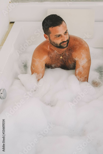 Hombre latino de mediana edad disfrutando de un baño con espuma y burbujas photo