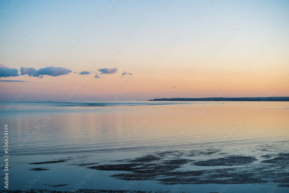 Obraz premium A beautiful calm sea at dusk. The light is delicate and golden. The water at low tide has gently ripples. The pier at Deal can be seen on the horizon.