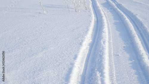 Track of traces from a snowmobile in drifts of white snow. Nature and outdoor. Winter theme wallpaper or background with snowy field