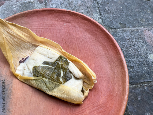 One Oaxacan tamale with hoja santa wrapped on the outside of the masa and filled with beans with brick background photo