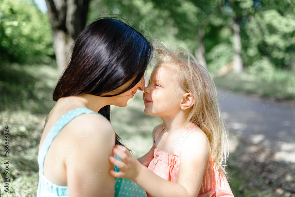 Mom brunette and daughter blonde laugh and touch each other's noses. Games for parents and children. Happy childhood, friendship and harmony in the family. Mom brunette and daughter blonde laugh and touch each other's noses. Games for parents and children. Happy childhood, friendship and harmony in the family.