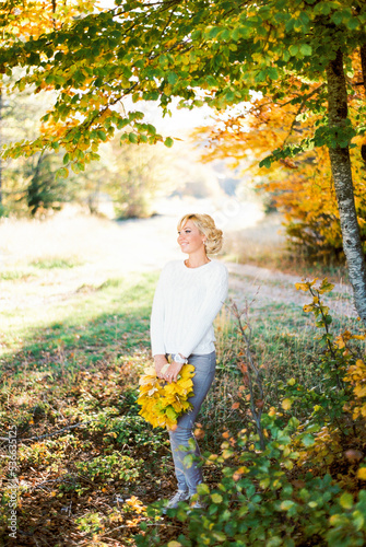 Happy woman with a bouquet of yellow leaves stands by a tree