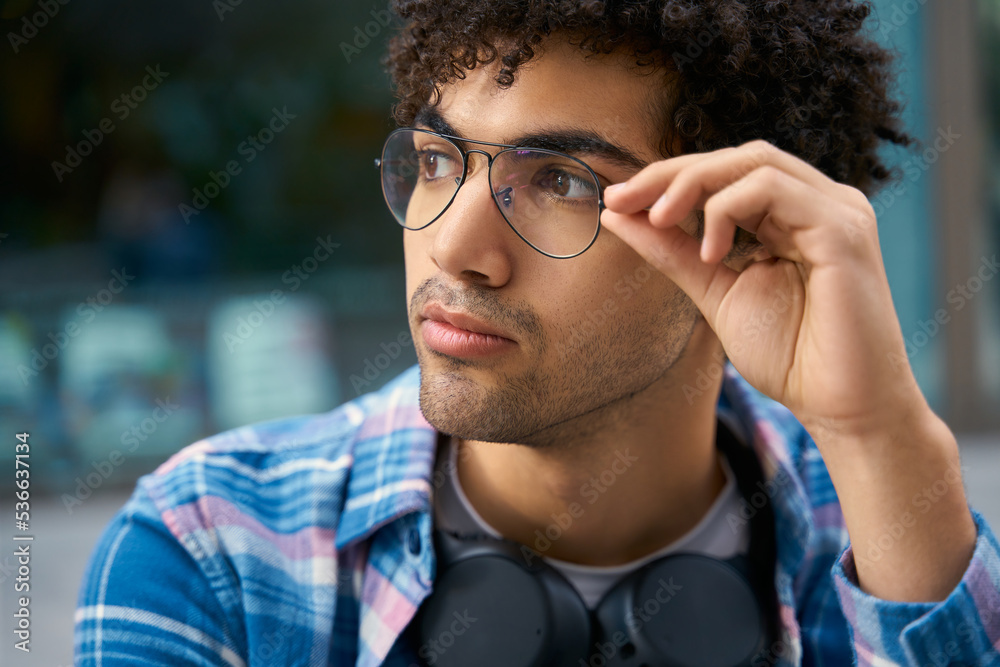 Portrait of handsome middle eastern man wearing eyeglasses looking away sitting on street. Young hipster student enjoying leisure outdoors Portrait of handsome middle eastern man wearing eyeglasses looking away sitting on street. Young hipster student enjoying leisure outdoors