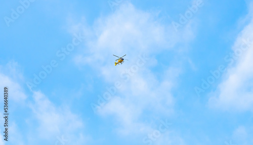 A yellow helicopter is flying high in the clear blue sky.