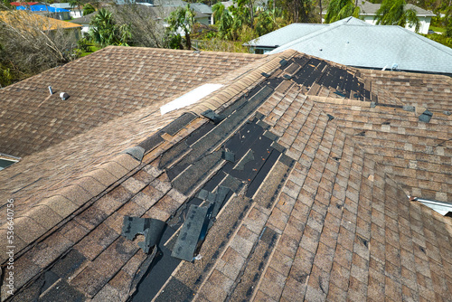 Damaged house roof with missing shingles after hurricane Ian in Florida. Consequences of natural disaster