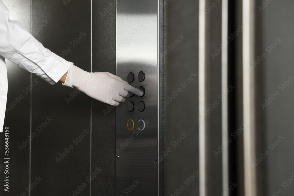 Woman wearing medical glove choosing floor in elevator, closeup. Protective measure