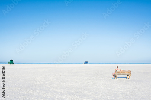 A woman is sitting on the bench and looking at the empty beach and ocean