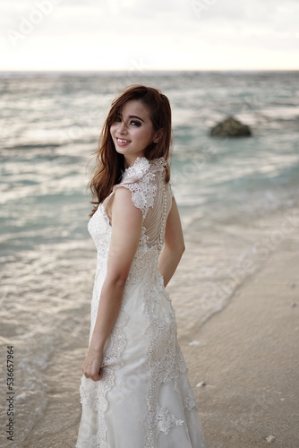 a caucassian woman is wearing white wedding dress with loose hairstyle having photo session in the beach