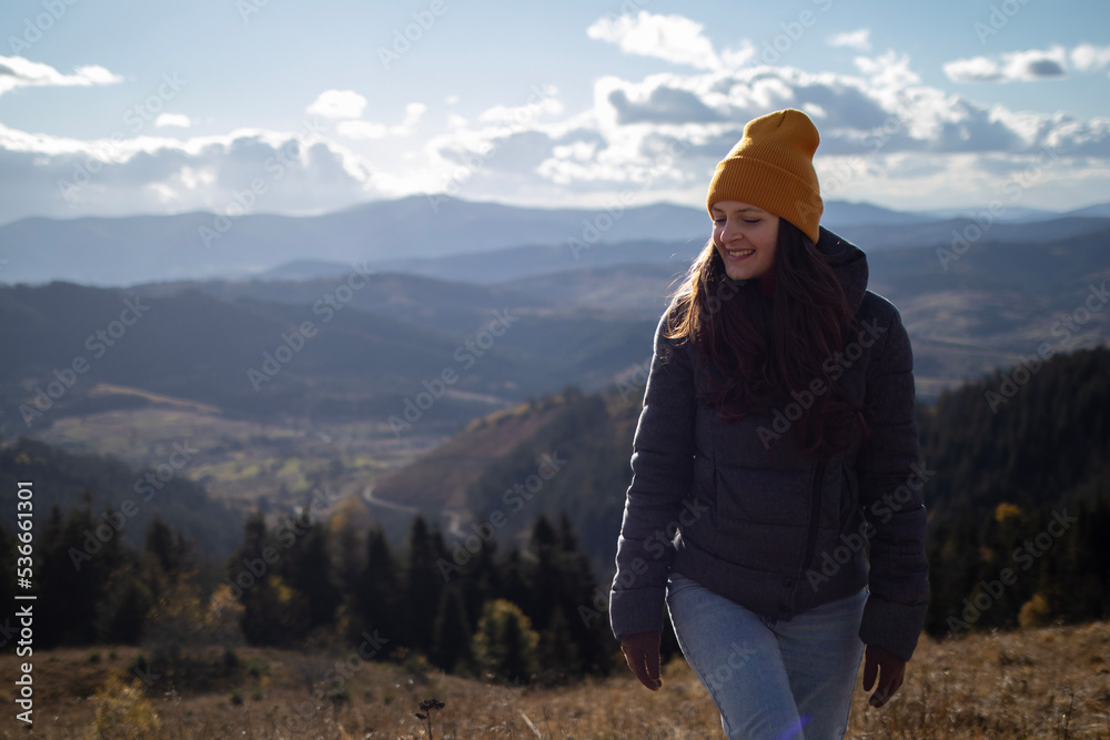 Young happy woman in orange beanie is walking in front of mountains landscape Young happy woman in orange beanie is walking in front of mountains landscape
