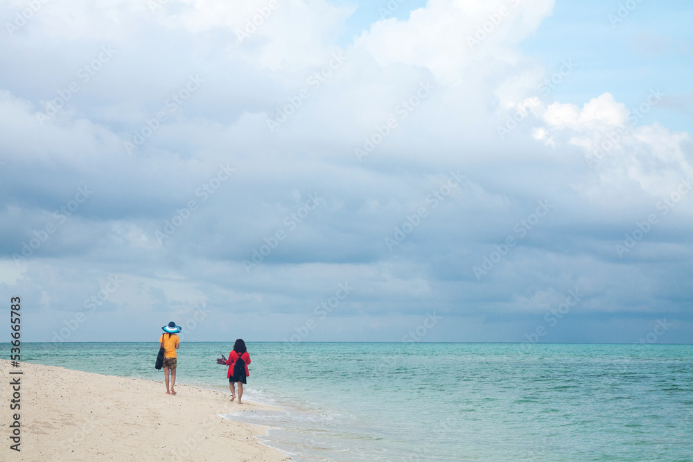 two women are walking along the beach while enjoying the beautiful view of the cloudy sky and the clear turquoise water