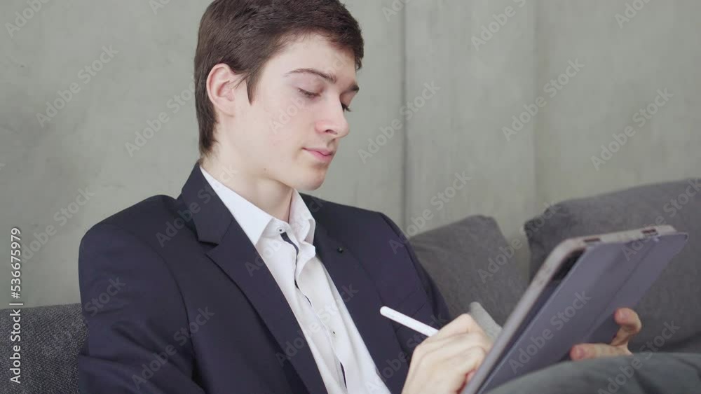 Young man working on tablet with isolate background. businessman wear suit, sit on sofa and using tablet in hotel Young man working on tablet with isolate background. businessman wear suit, sit on sofa and using tablet in hotel