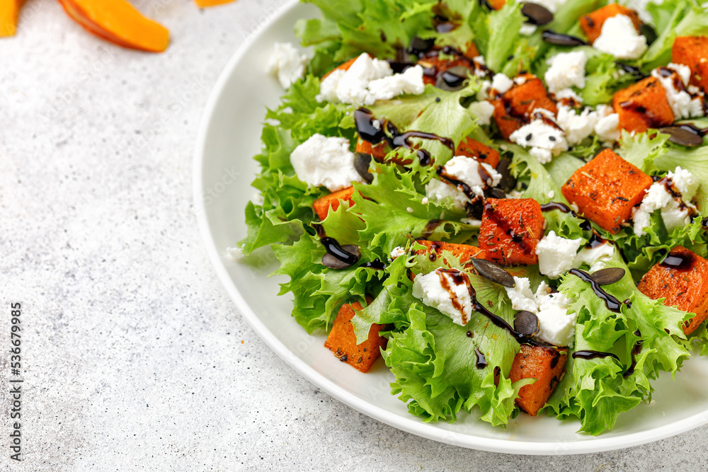 Pumpkin salad with green lettuce, feta cheese, balsamic sauce. Autumn healthy salad with roasted baked pumpkin on white plate.