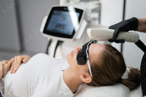 Young caucasian woman in goggles on photorejuvenation procedure. Portrait of a girl in a beautician's clinic.