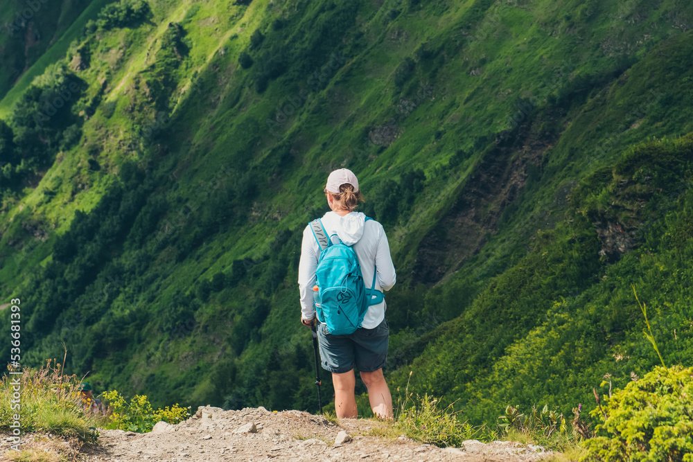 A female traveler with backpack on the top of a mountain. Mountain peaks. Krasnaya Polyana, Sochi, Russia. Climbing the mountain.