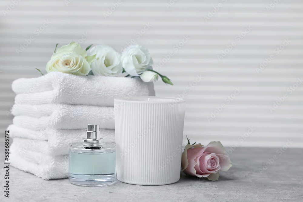 Towels, bottle of perfume, scented candle and flowers on grey table indoors