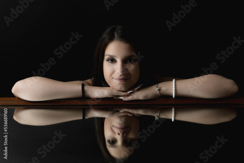 Low key portrait of brunette young woman lying on the mirror. Horizontally. 