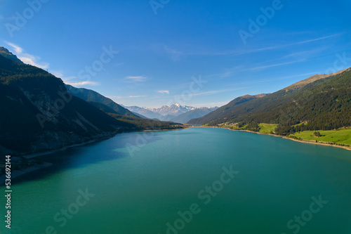 Aerial view of lake (Reschensee). Large reservoir surrounded by mountains at sunny noon. Recreation area for tourists and sportsmen. Italy, Vinschgau.