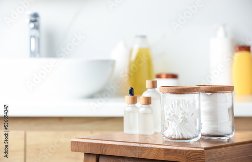 Cotton pads and swabs near cosmetic products on wooden stool in bathroom. Space for text