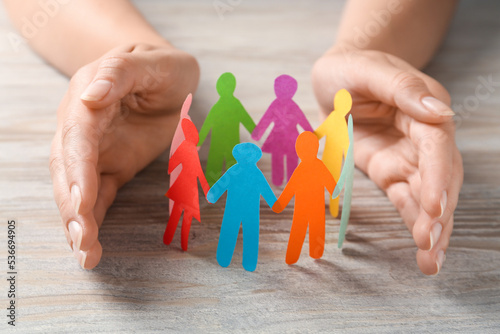 Foto Woman protecting paper human figures on wooden table, closeup