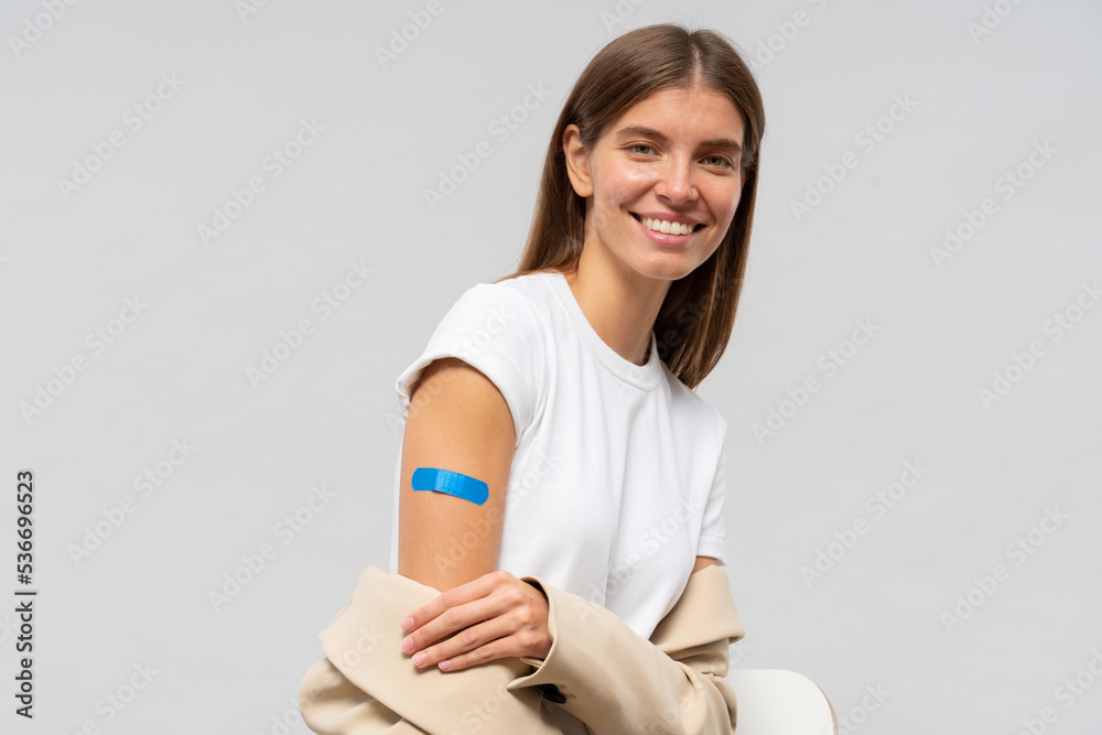 Vaccinated woman smiling after getting vaccine shot showing shoulder with blue bandage Vaccinated woman smiling after getting vaccine shot showing shoulder with blue bandage