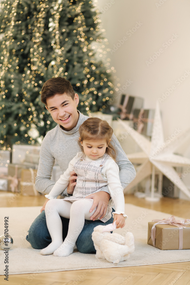 Happy young boy with his niece play in front of fir tree. Christmas mood Happy young boy with his niece play in front of fir tree. Christmas mood