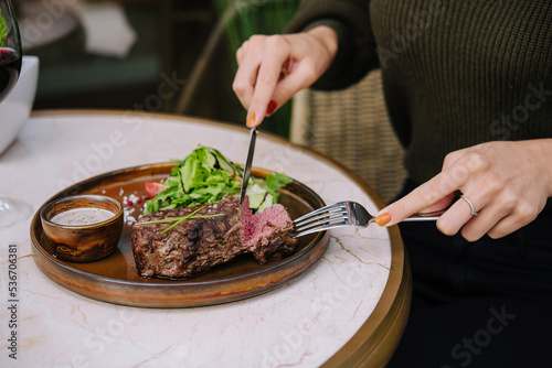female hands in a restaurant at the table cut beef striploin steak