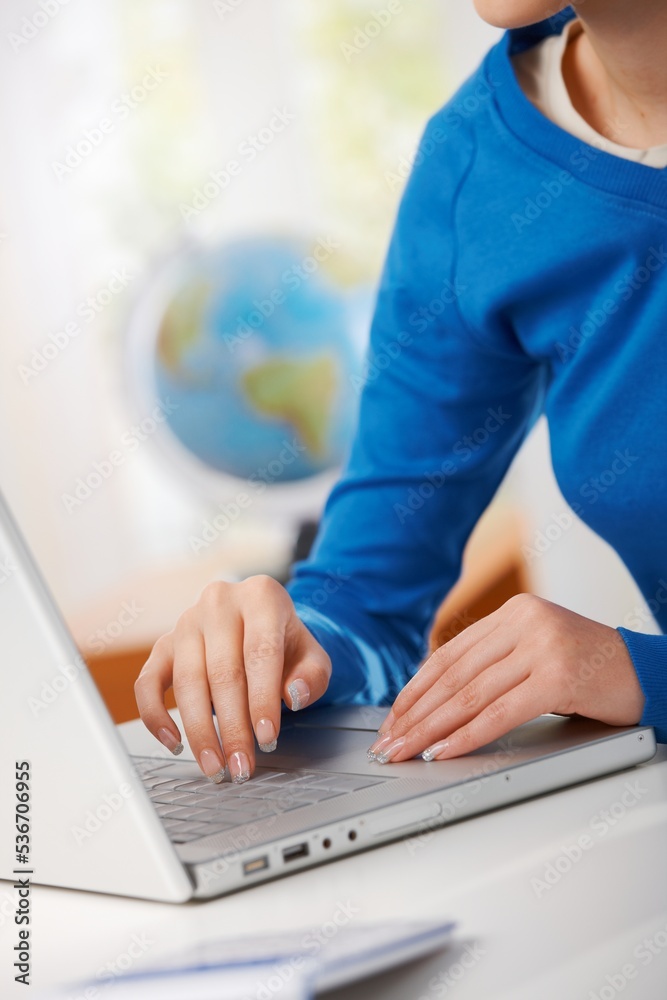 Naklejka premium Female hand typing on laptop computer keyboard, globe in background.