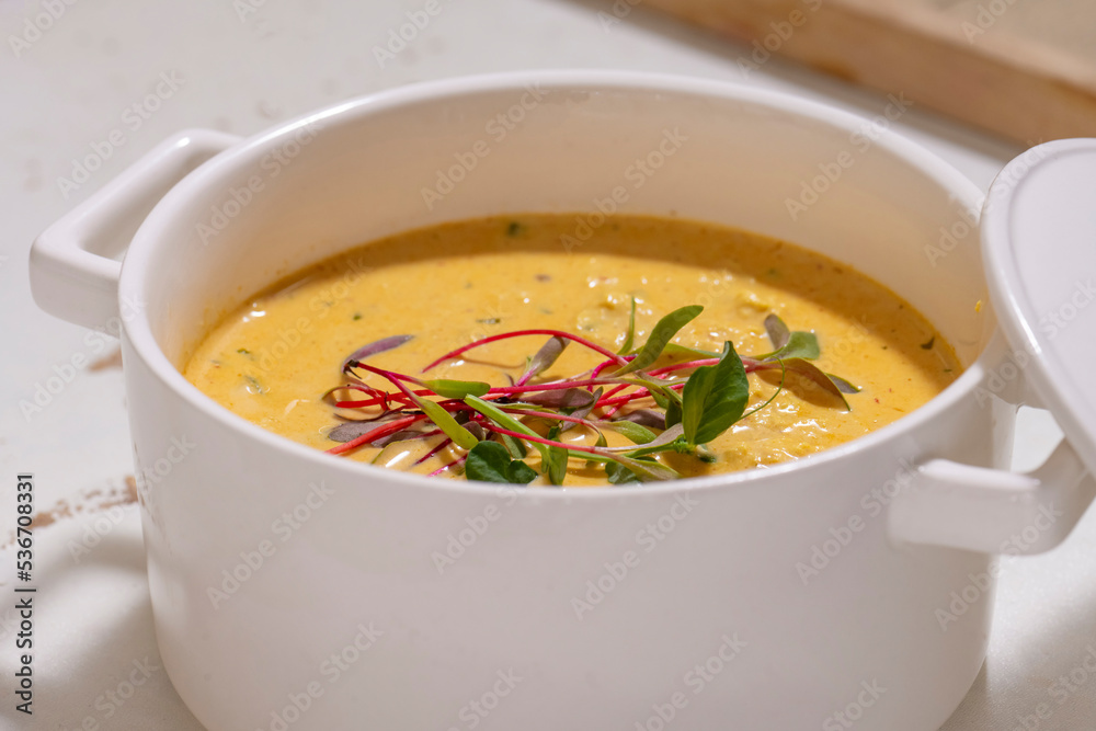 Pumpkin cream soup served with herbs in ceramic pot with lid Pumpkin cream soup served with herbs in ceramic pot with lid